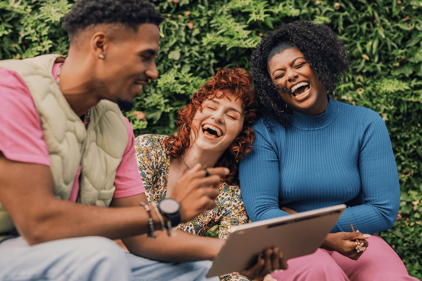 Three people laughing together while looking at a tablet